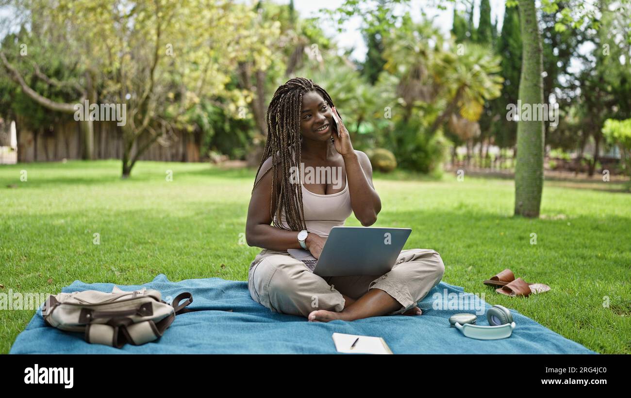 African american woman student using laptop talking on smartphone at ...