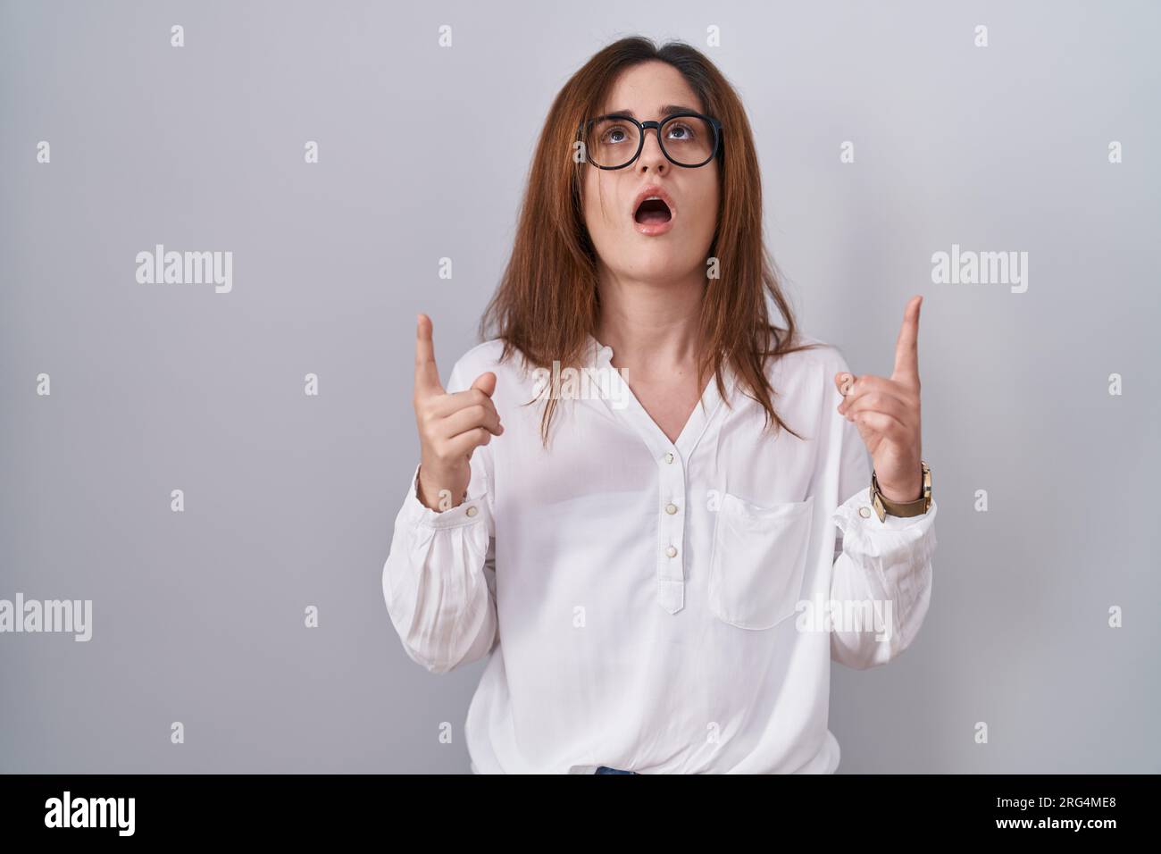 Brunette woman standing over white isolated background amazed and ...