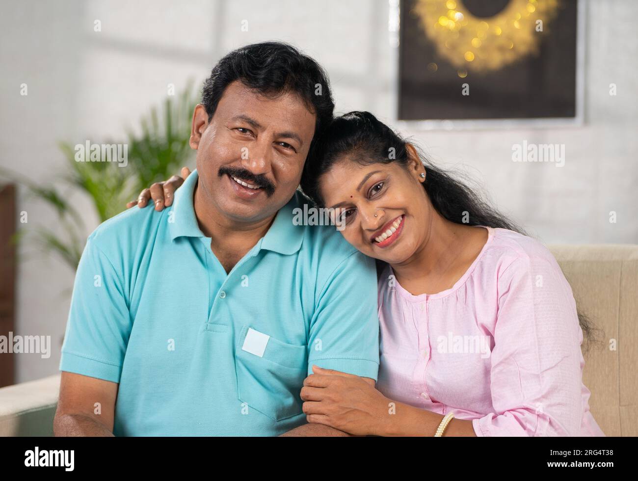 Happy middle aged indian couple looking at camera while sitting on sofa ...