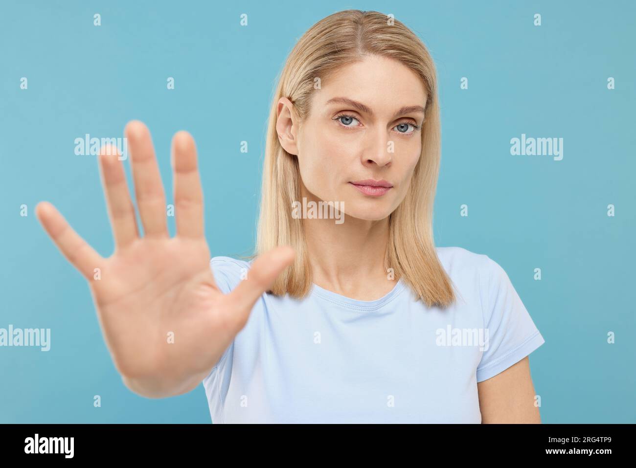 Woman showing stop gesture on light blue background Stock Photo - Alamy