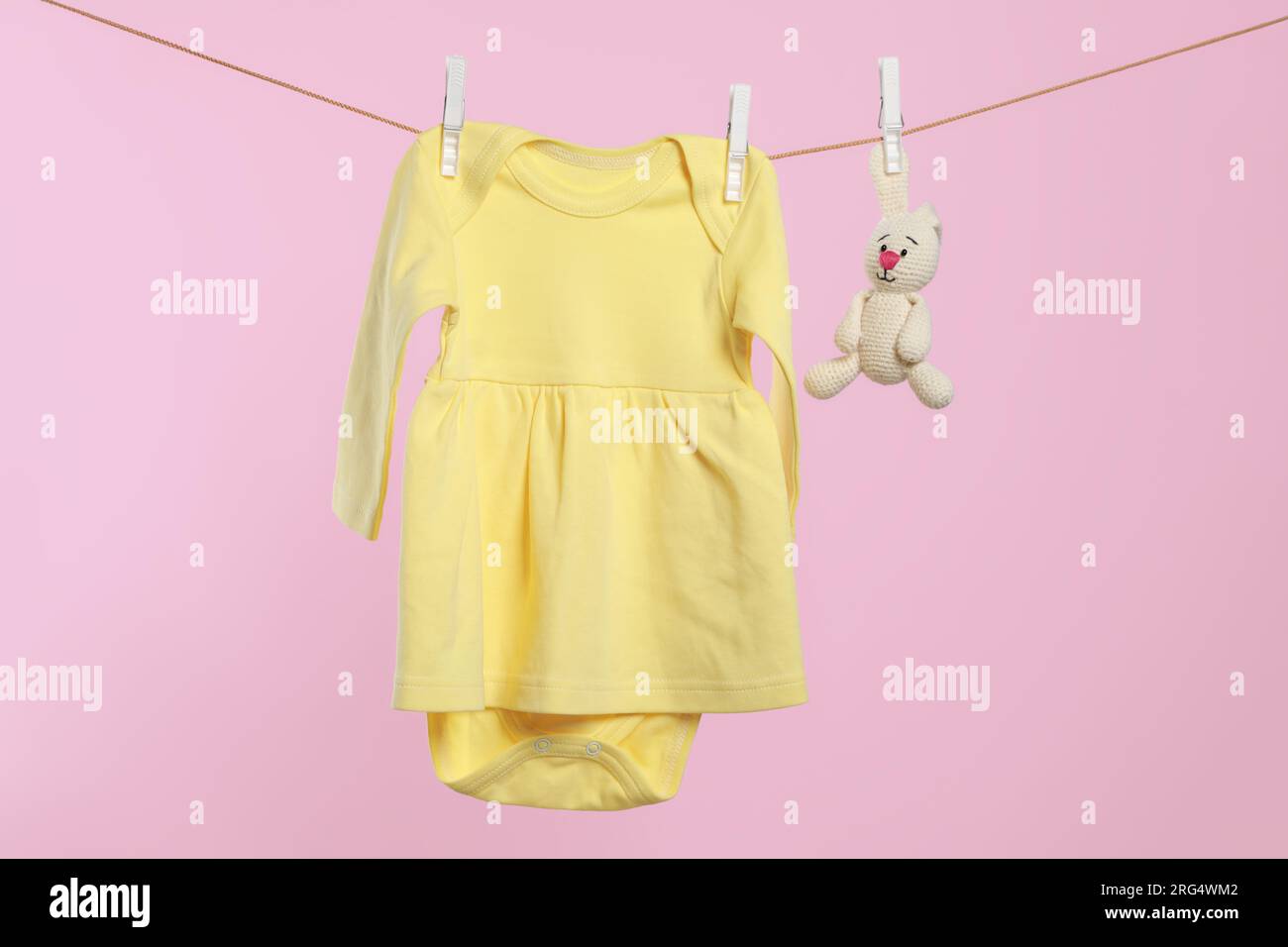 Yellow baby dress and crochet toy drying on washing line against pink