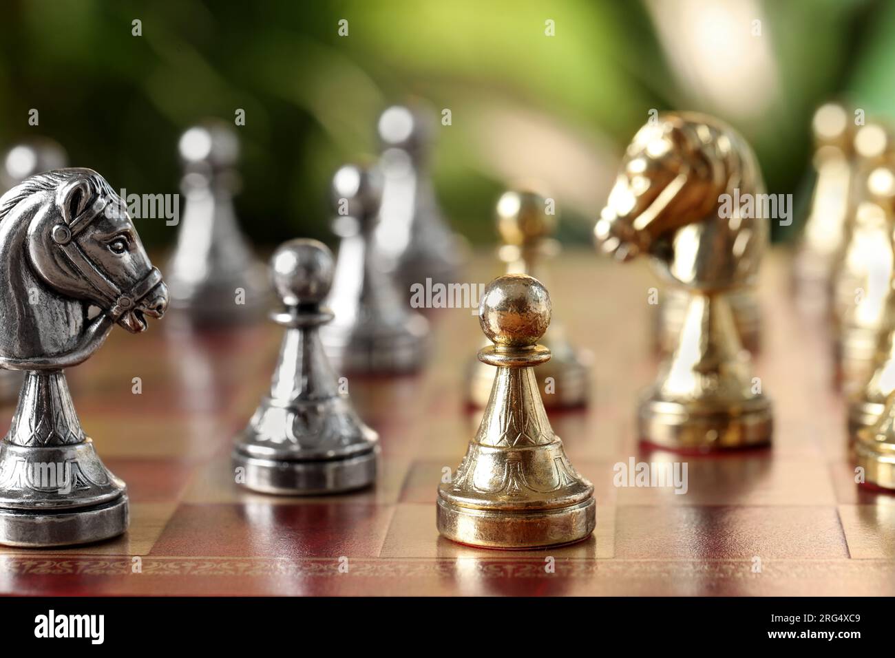 Golden pawn and silver knight on chess board against blurred background, closeup Stock Photo