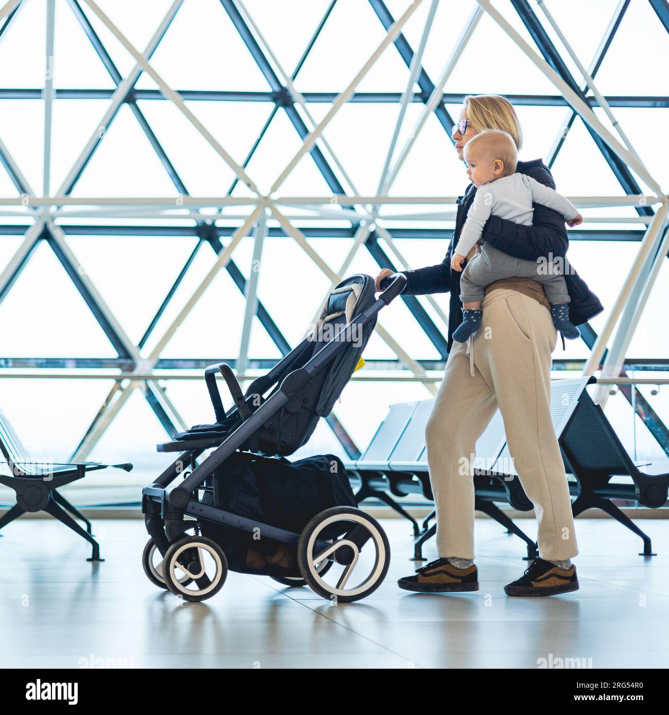Mother carying his infant baby boy child, pushing stroller at airport