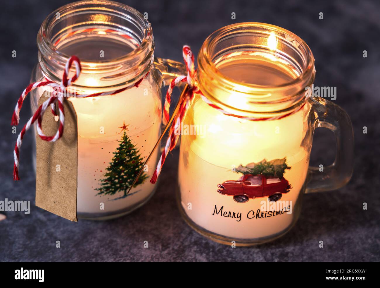 Christmas candles of white paraffin in a glass, decorated with a car and a Christmas tree on a gray background. Stock Photo