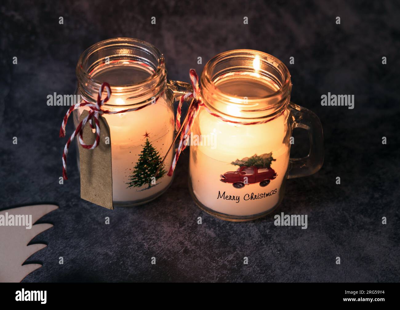 Christmas candles of white paraffin in a glass, decorated with a car and a Christmas tree on a gray background. Stock Photo