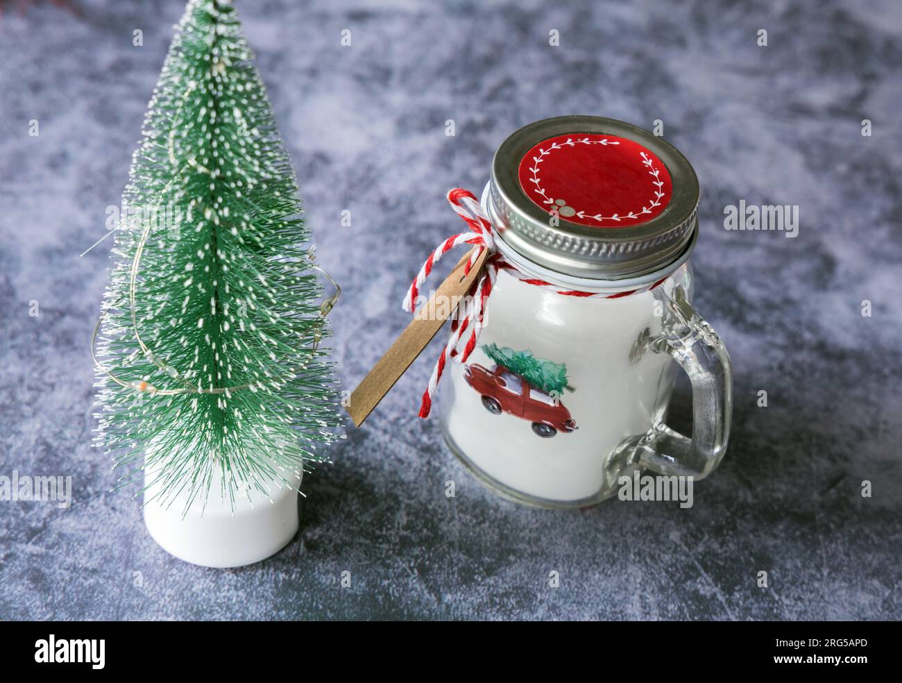 Christmas candles of white paraffin in a glass, decorated with a car and a Christmas tree on a gray background. Stock Photo
