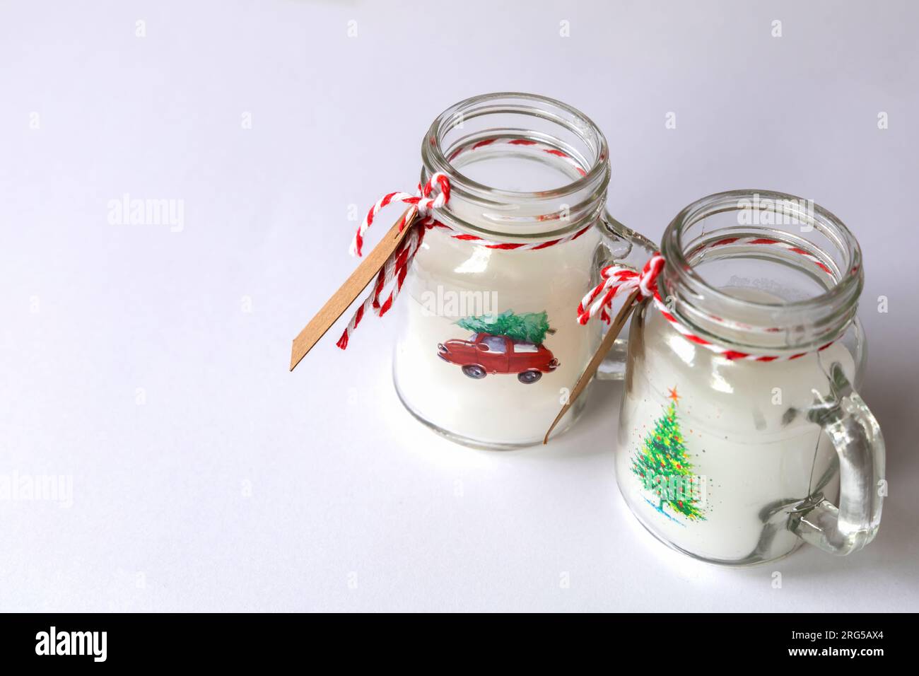 Christmas candles of white paraffin in a glass, decorated with a car and a Christmas tree on a gray background. Stock Photo