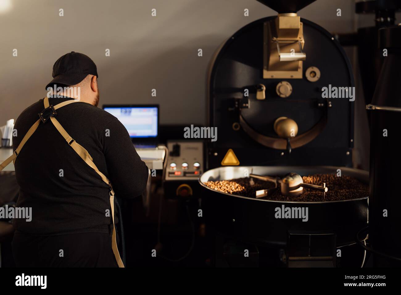 Man using laptop while working with coffee roasting machine Stock Photo