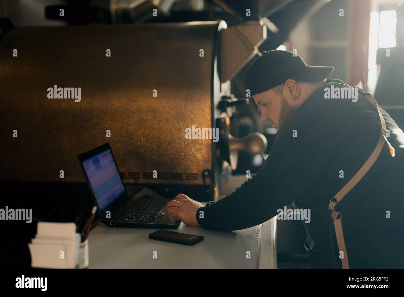 Man using laptop while working with coffee roasting machine Stock Photo