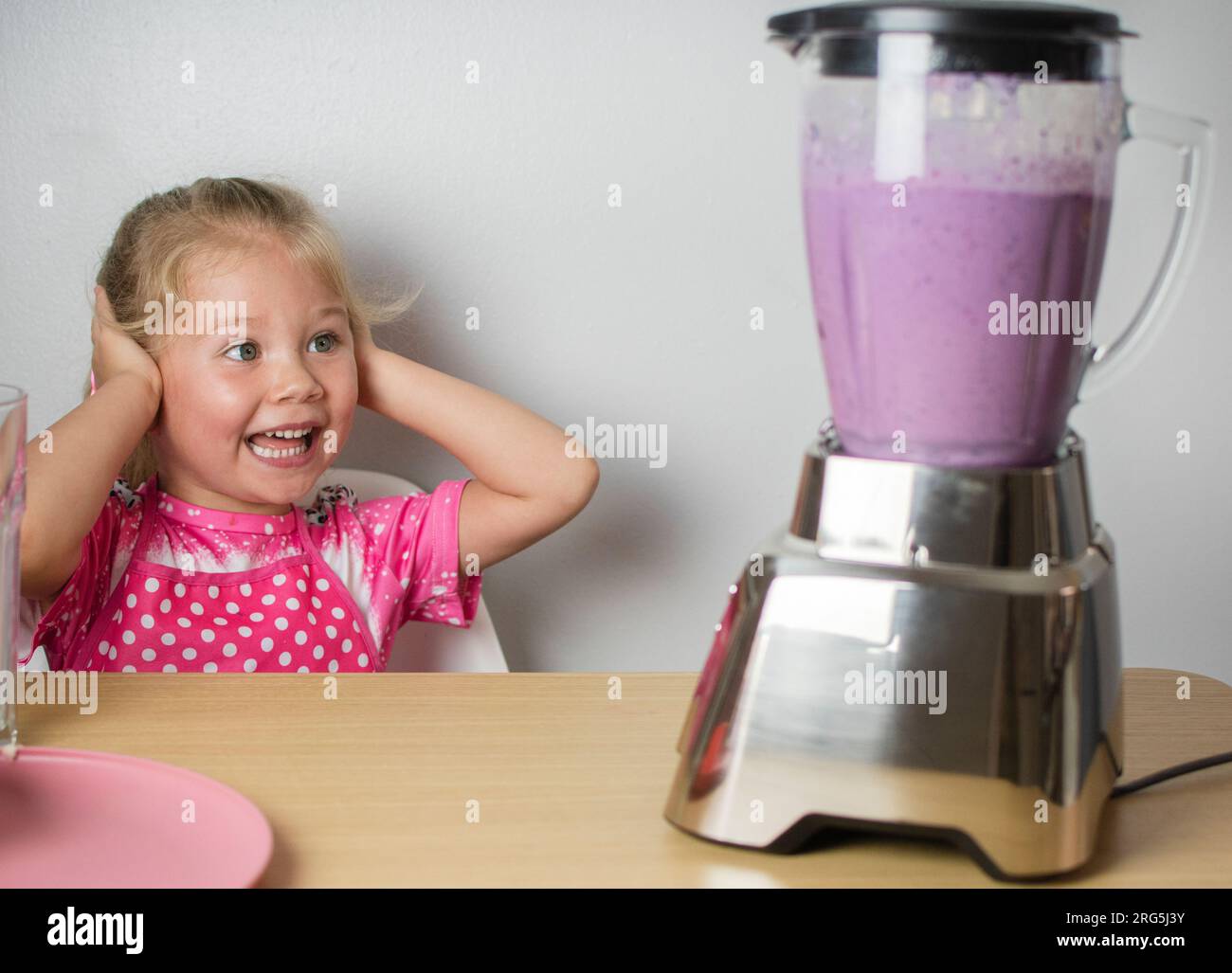 Happy Caucasian cute child is amused by loud sound of the blender
