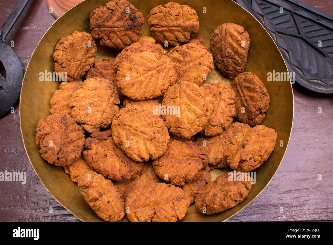 Thekua , an Indian sweet dish or a snacks in a brass plate with mold in wooden table. It is popular in bihar and jharkhand .Prashad in chhath festival Stock Photo