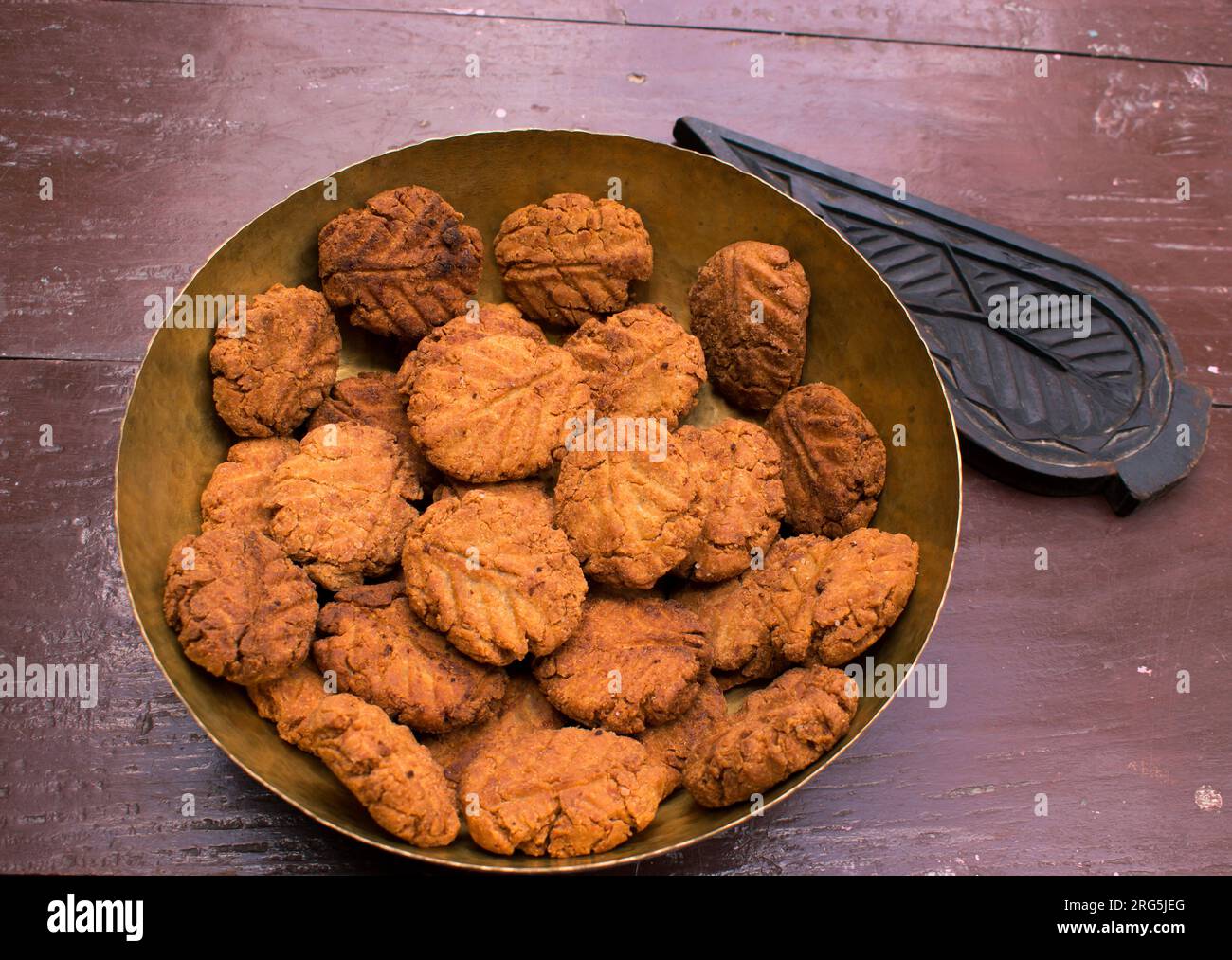Thekua , an Indian sweet dish or a snacks in a brass plate with mold in wooden table. It is popular in bihar and jharkhand .Prashad in chhath festival Stock Photo