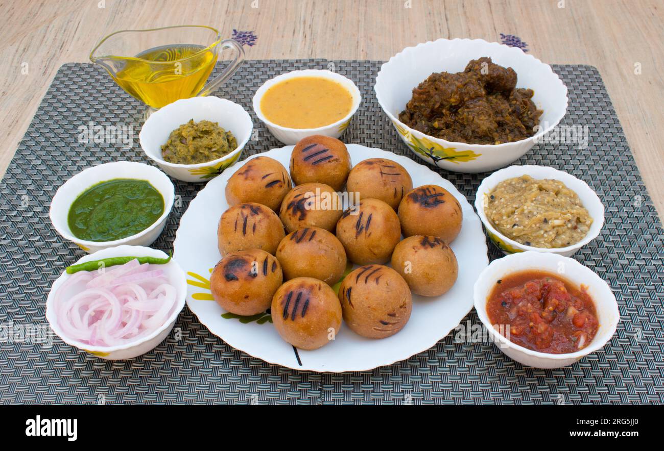Litti in white plate with tomato, brinjal, potato, pointed gaurd and coriander chutney or chokha and ghee. It is popular in Bihar, Uttar Pradesh Stock Photo