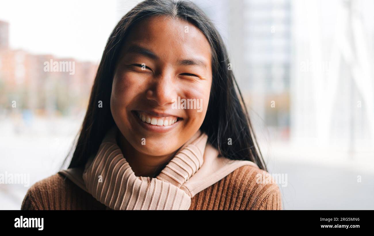 Authentic portrait of Asian woman smiling on camera with city background - Youth culture concept Stock Photo
