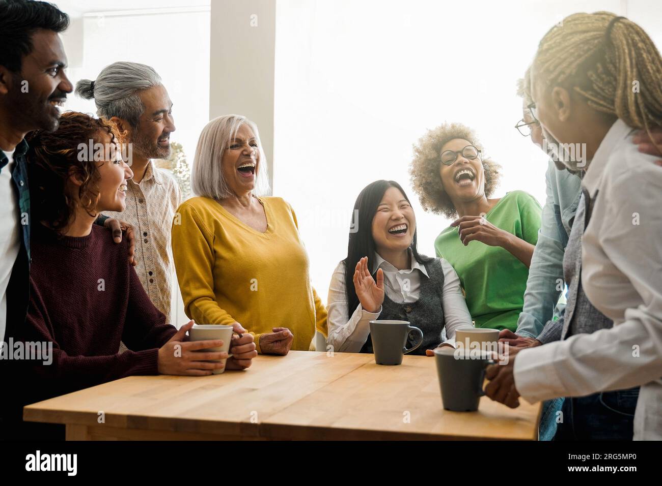Happy multiethnic people drinking tea during lunch break at work - Group of multi-generational friends having fun laughing together - Soft focus on As Stock Photo