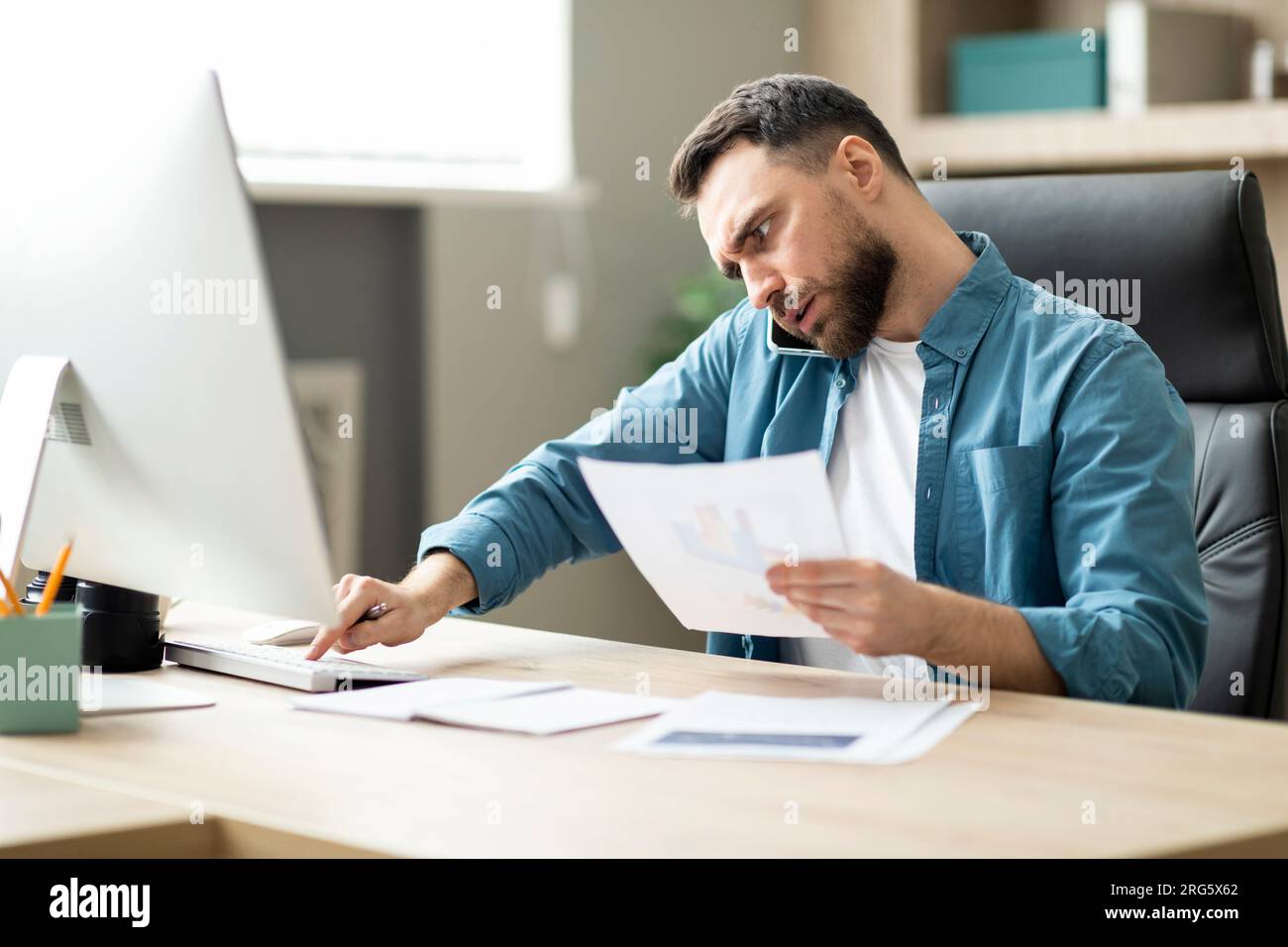 Multitasking. Young Businessman Working On Computer, Talking On Cellphone And Checking Documents Stock Photo