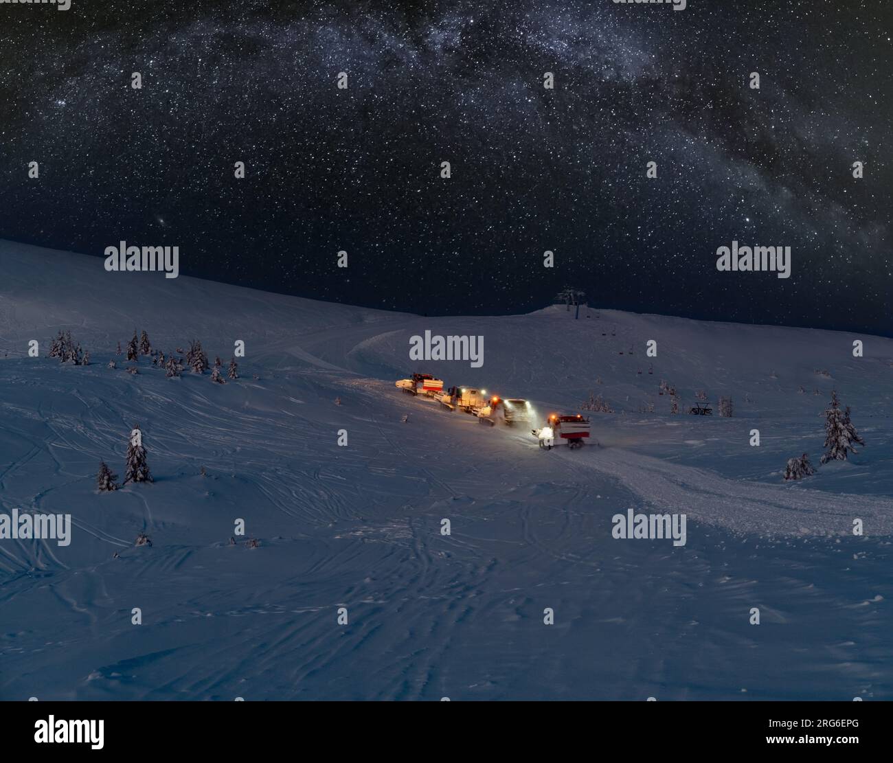 Snow groomers (snowcat ratrack machines) on night  excursion ride to winter mountain top with freeriders snowboarders and starry sky with Milkyway abo Stock Photo