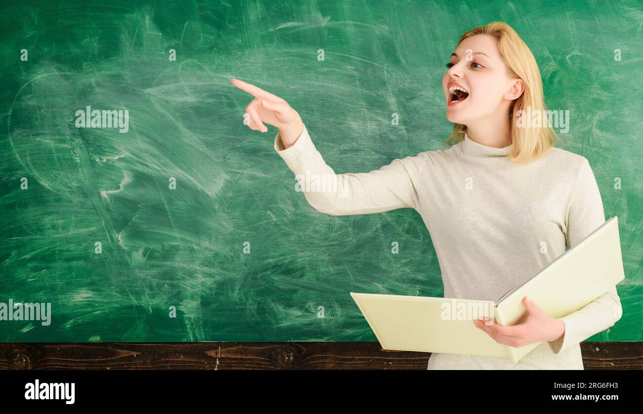 High school teacher near chalkboard in classroom. Happy female teacher giving lesson to students in school or university. College student girl or Stock Photo