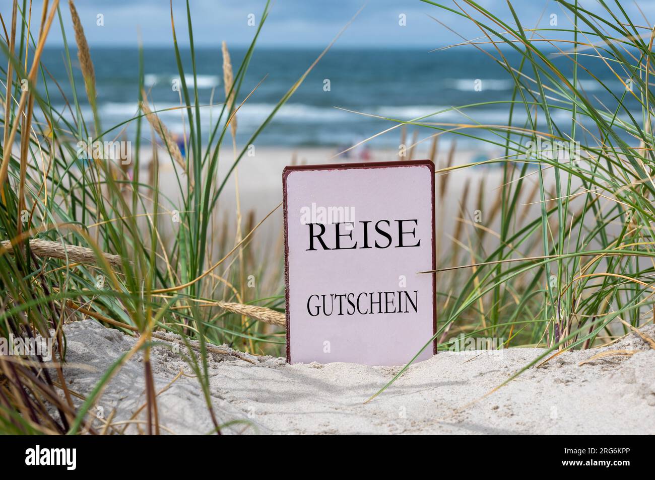 The German text 'Reise Gutschein' (travel voucher) in the sand dunes at the beach. Stock Photo