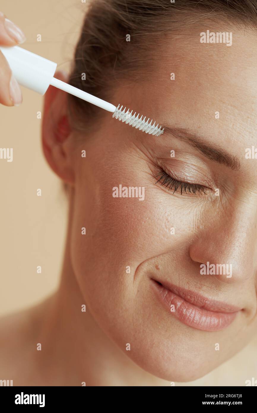 Closeup on young female with brow brush on beige background. Stock Photo