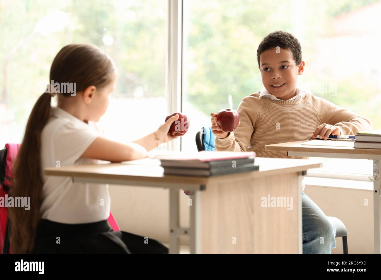 Little students with apples sitting at desks in classroom Stock Photo