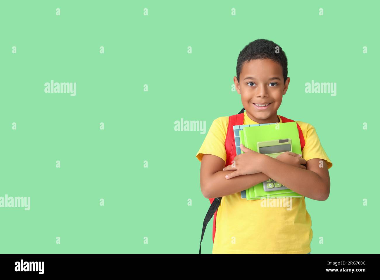 Little African-American boy with backpack and school supplies on green ...