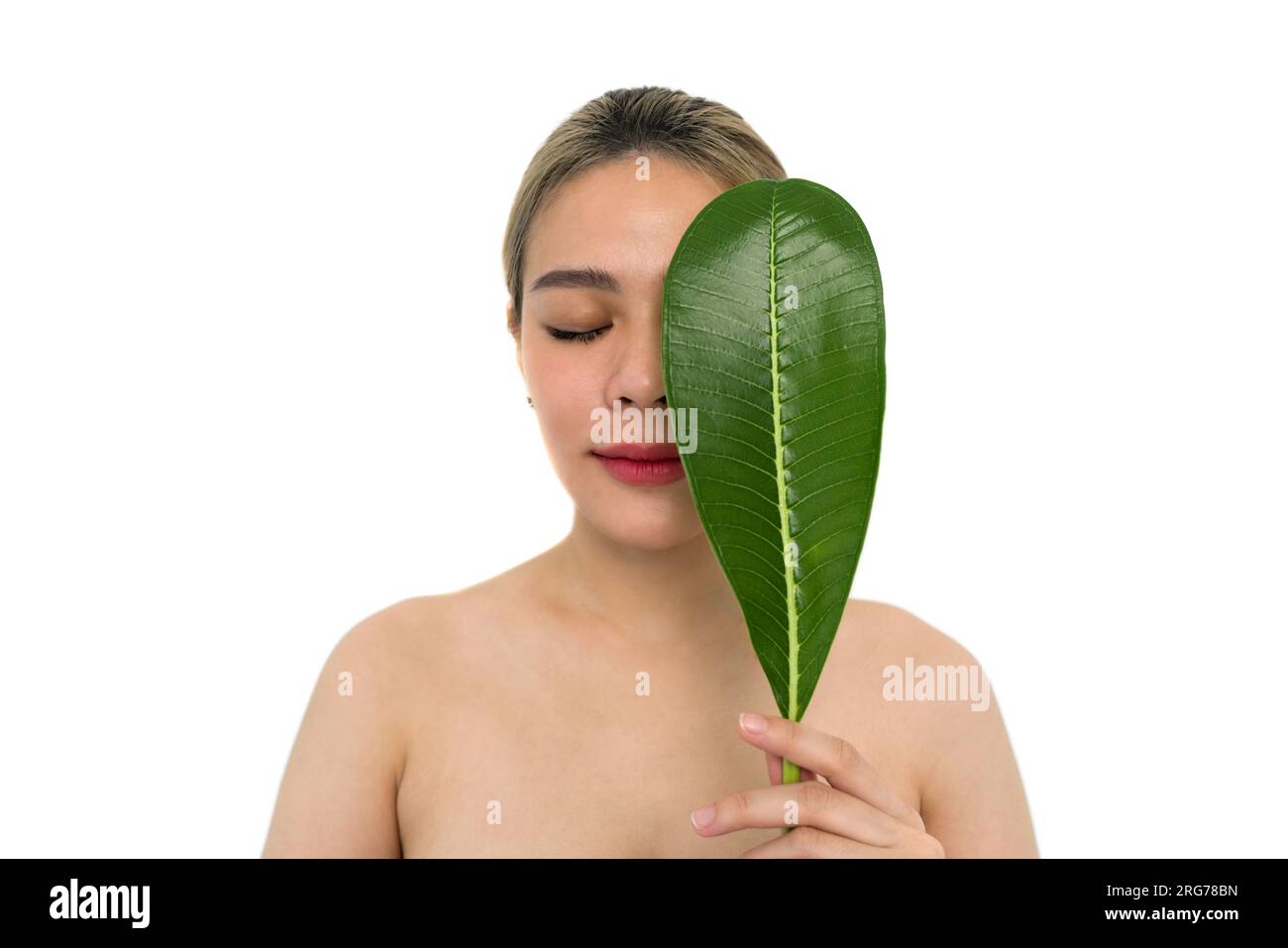 Young asian woman playfully covering her face with a vibrant green leaf ...