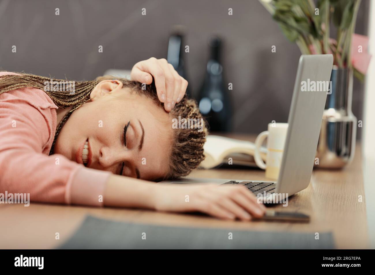 Exhausted from work or studying, a woman with box-braids falls asleep at her laptop, hand on phone Stock Photo