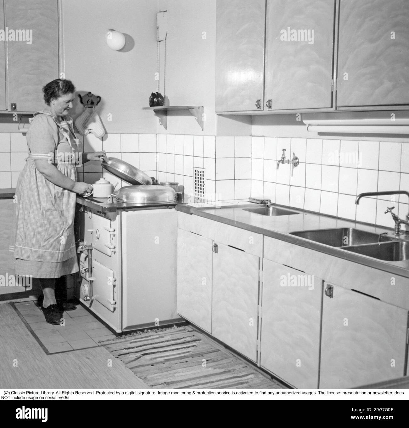 The AGA cooker. A swedish invention by Gustaf Dalén with the principle of heat storage, a combination of two large hotplates and two ovens into one unit, the AGA cooker. The oldest AGA cooker still in use belongs to the Hett family of Sussex and it was installed 1932. This picture was taken 1950 Mrs Ester Lundberg is seen making coffee on the stove. Stock Photo