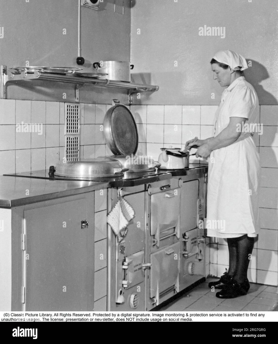 The AGA cooker. A swedish invention by Gustaf Dalén with the principle of heat storage, a combination of two large hotplates and two ovens into one unit, the AGA cooker. The oldest AGA cooker still in use belongs to the Hett family of Sussex and it was installed 1932. This picture was taken 1950 where a woman is seen cooking something on the stove. Sweden Stock Photo