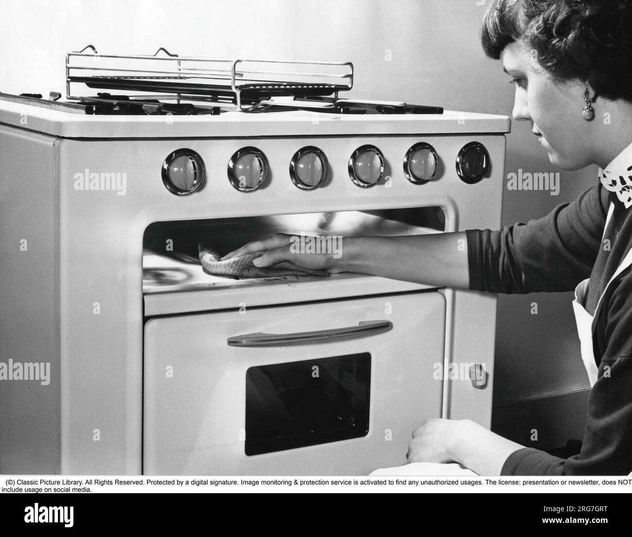 In the kitchen in the 1950s. A young woman in the kitchen at the brand new Kockums gas cooker. She is seen demonstrating the practical function of having a enameled spill plate under the burners and how easy it is to clean even from the largest boil-overs. Sweden 1956. Stock Photo