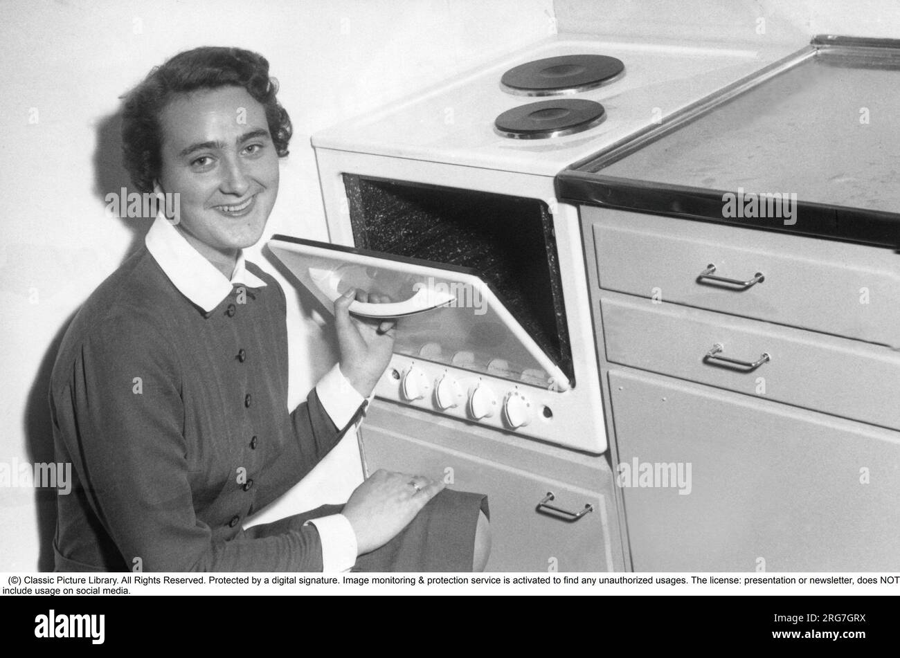 In the kitchen in the 1950s. A young woman in the kitchen at a seemingly brand new electric cooker with an integrated oven. Small and practical suitable for a smaller kitchen. Sweden 1954 Stock Photo
