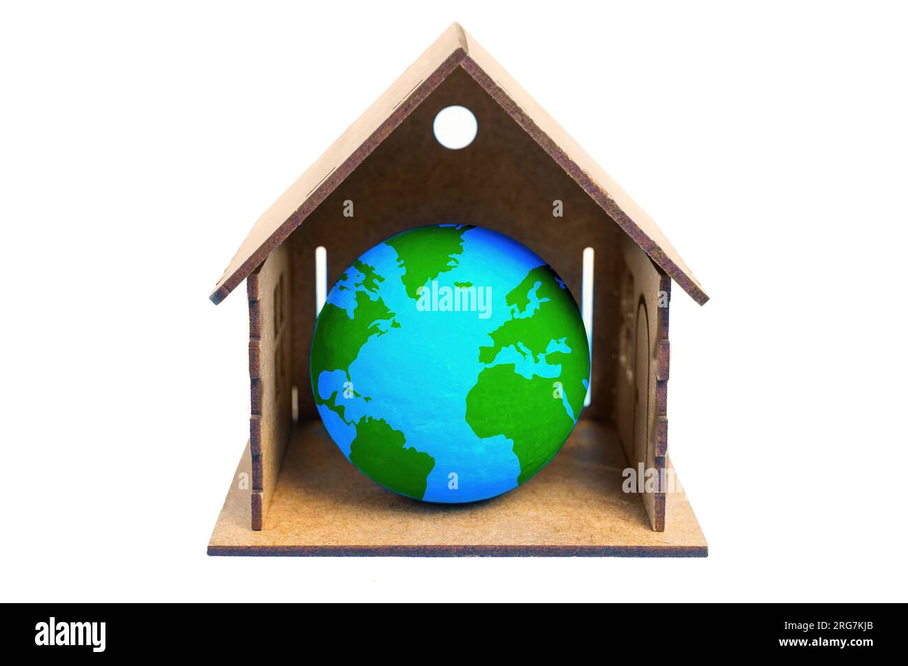 Close-up of a tiny green and blue globe nestled inside a miniature wooden house isolated on white background. Global awareness and responsible steward Stock Photo