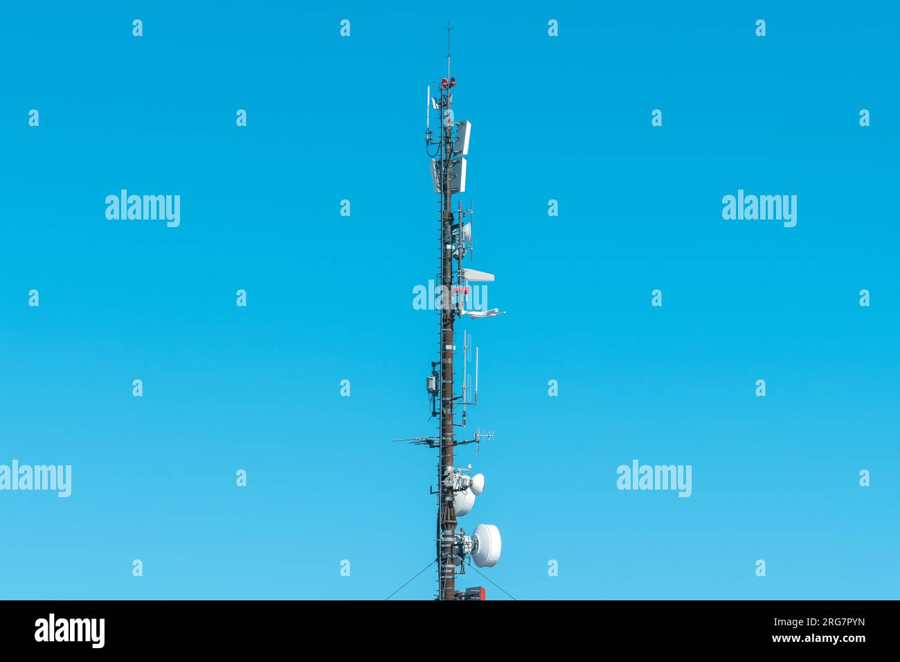 Large telecommunication tower with antennas and satellite dishes, mobile telephony signal repeaters and 4g transmitters and emitters against blue sky Stock Photo