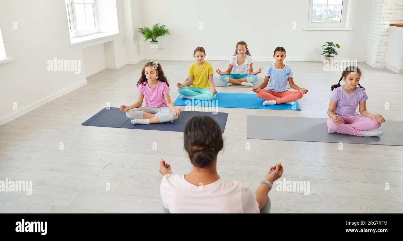 Group of children having a yoga class, sitting on mats, doing relaxing ...