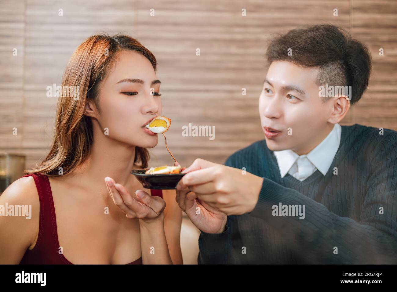 Young asian man feeding happy girlfriend with tasty food in restaurant Stock Photo