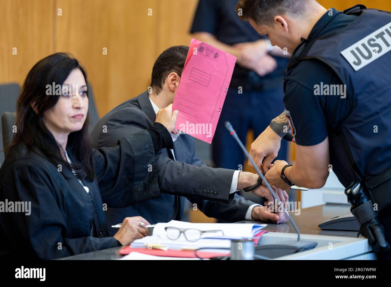 Essen, Germany. 08th Aug, 2023. A court official removes the handcuffs from  the defendant, his lawyer Simone Dahlmann-Ludwig (l) holds a red folder in  front of his face. The trial of the