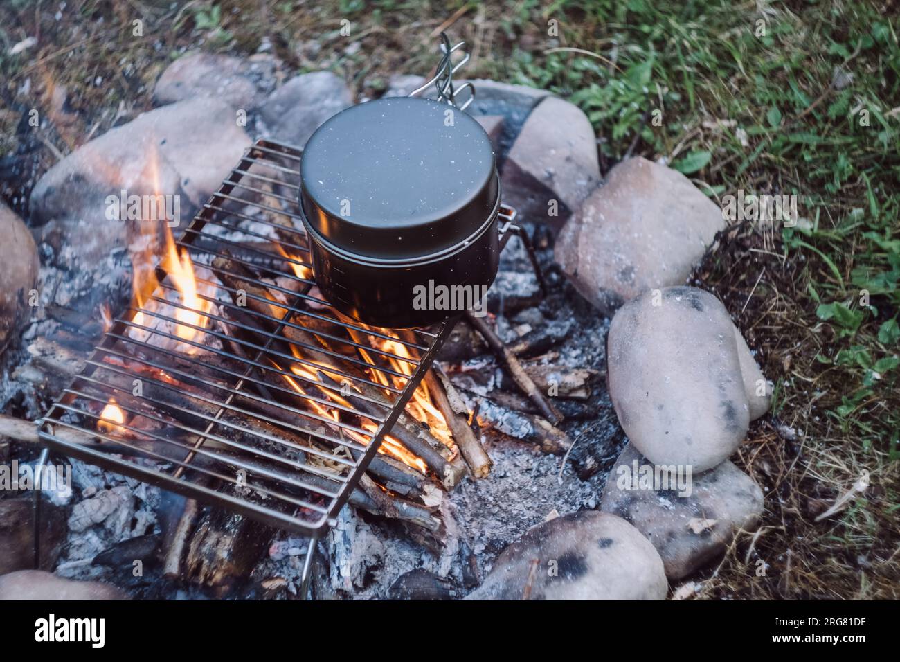 Close-up top view of one black pot above beautiful calm campfire at evening time. Bonfire cooking in warm night time. Camping vibes, nature and outdoo Stock Photo