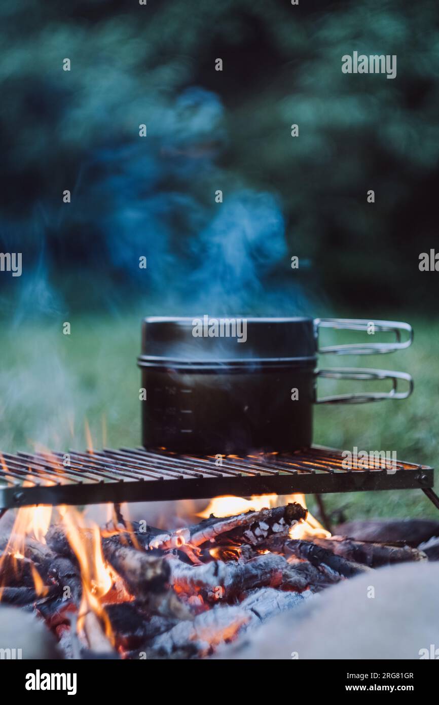 Close-up of black pot above beautiful calm campfire in evening. Bonfire cooking in warm night time. Camping vibes, nature and outdoor lifestyle mood c Stock Photo