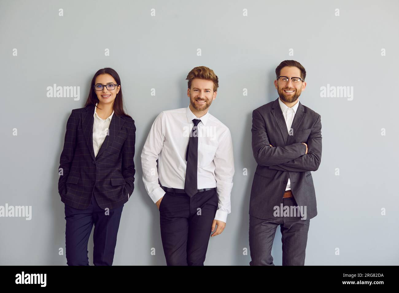 Team of happy young business people wearing formal office clothes standing by wall Stock Photo