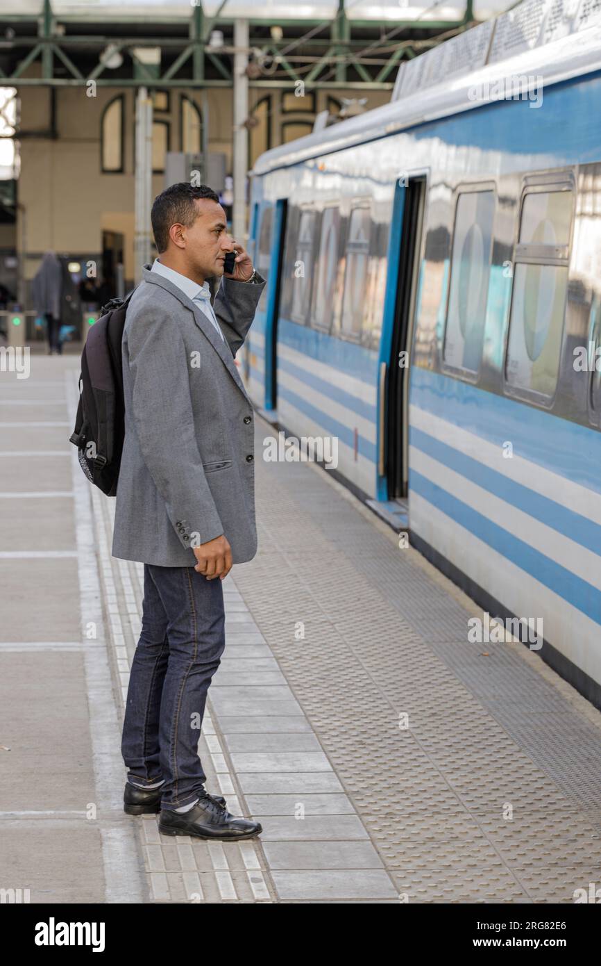 Young latin man talking on a mobile phone on the platform of a train station. Stock Photo