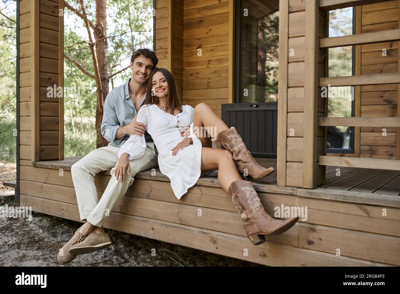 romantic getaway, man hugging cheerful woman while sitting together on porch of vacation house Stock Photo