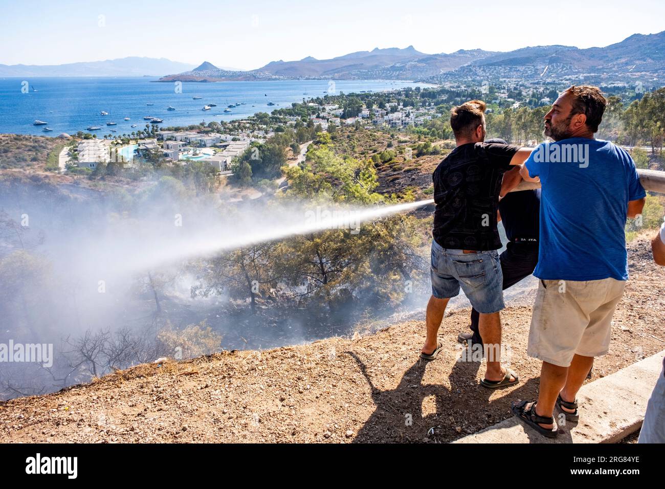 Bodrum,Turkey, 08.08.2023: Civil people holding water fire hose, helping firefighters in action. Fire disaster background with copy space. Stock Photo