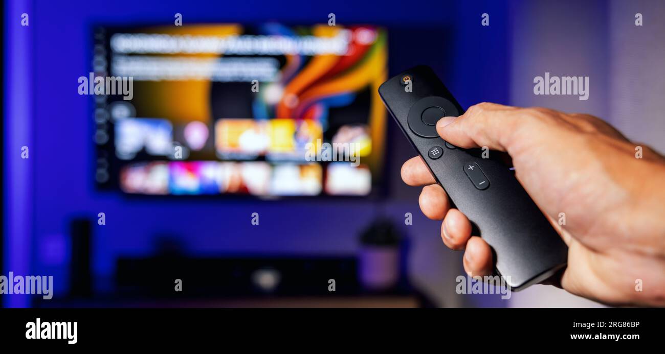 remote control in hand with tv in background at home. streaming service, content on demand. banner with copy space Stock Photo
