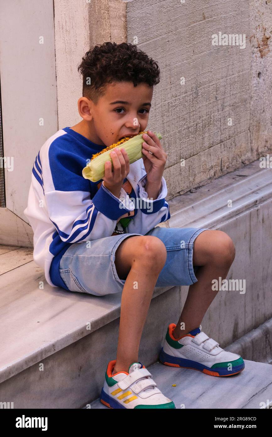 Istanbul, Turkey, Türkiye. Istiklal Street, Young Boy Eating Roasted Corn on the Cob. Stock Photo