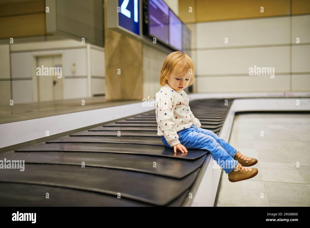 Adorable little girl in the airport. Toddler sitting on baggage carousel and waiting for luggage