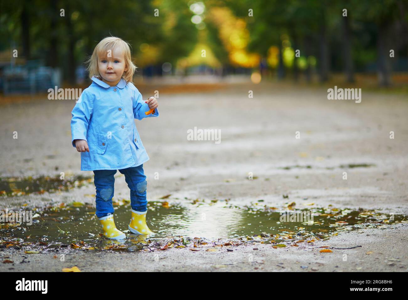 Child wearing yellow rain boots and jumping in puddle on a fall day ...