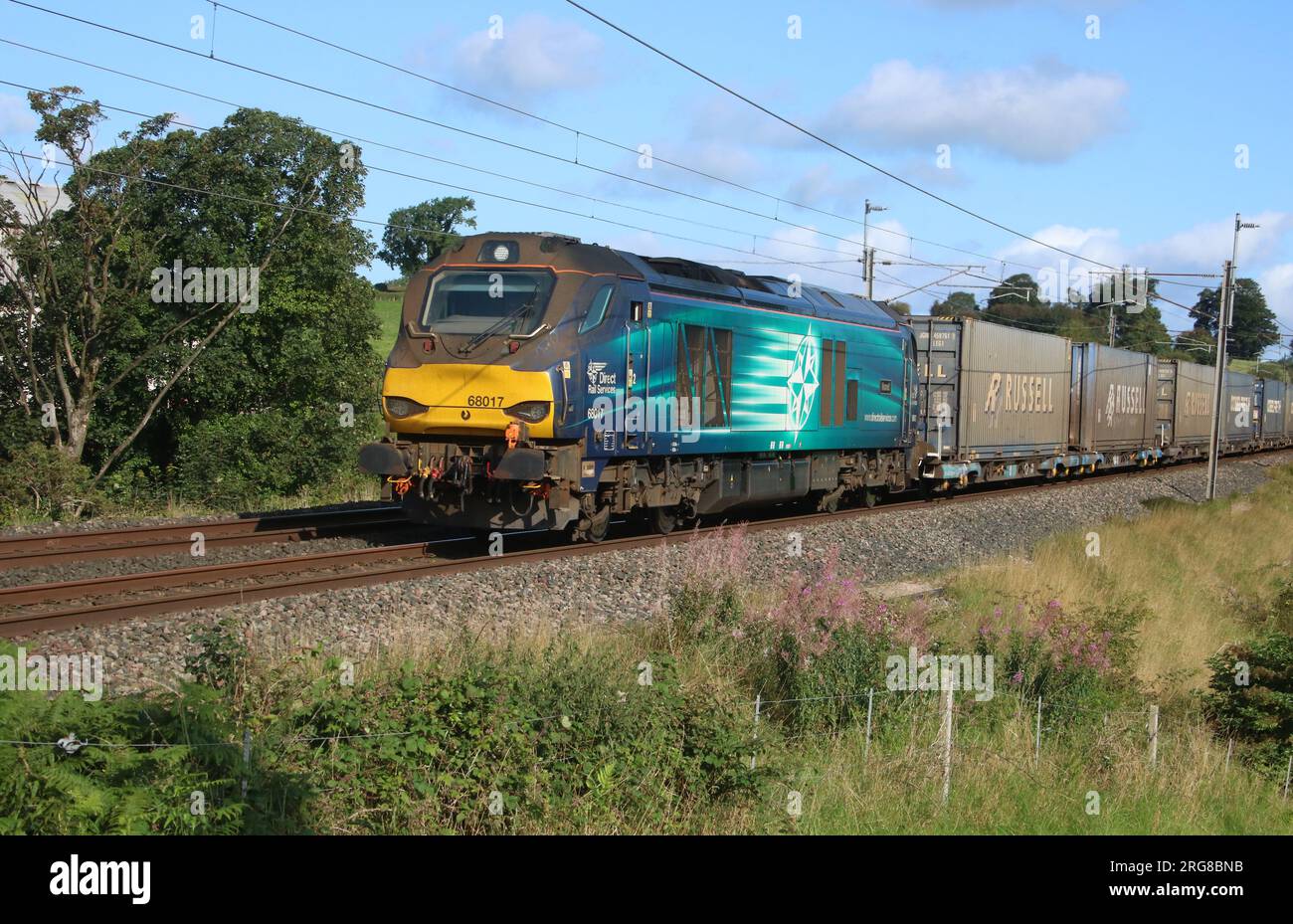 Direct Rail Services diesel-electric 68017 Hornet, passing Bay Horse in Lancashire on West Coast Main Line with container train on 8th August 2023. Stock Photo