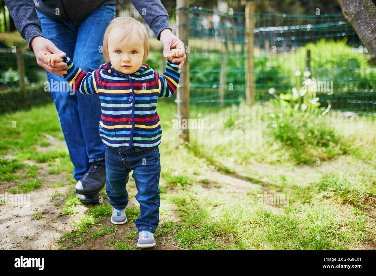 Man with 1 year old baby girl in park. Father helping his daughter make