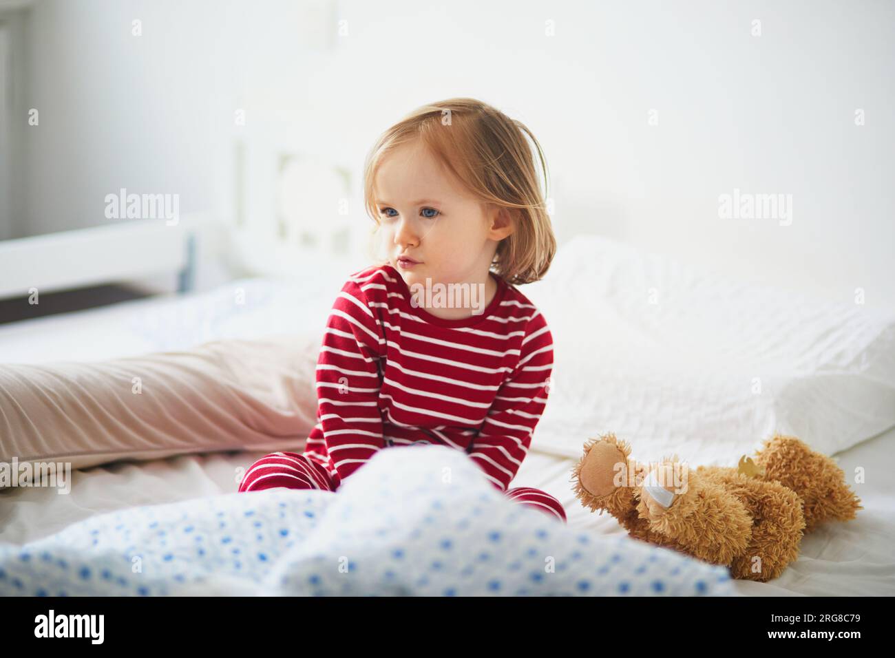 Toddler girl in striped red and white pajamas sitting on bed right